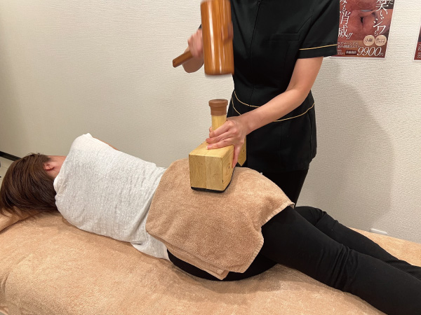 大阪平野区エステサロン、サラスバティの美容整体×EMS筋膜リリース施術写真、ハンマーで腰を整える、横向き